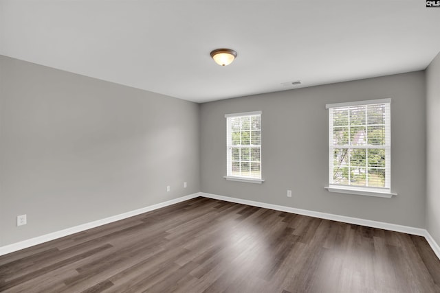 empty room featuring dark wood-style flooring, visible vents, and baseboards