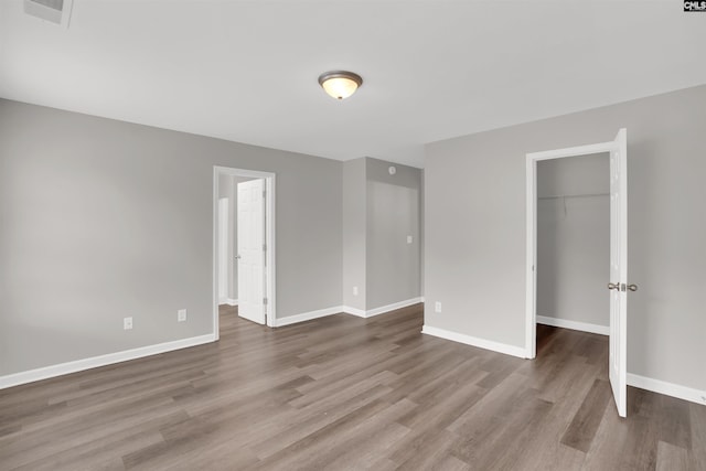unfurnished bedroom featuring baseboards, a spacious closet, wood finished floors, and a closet