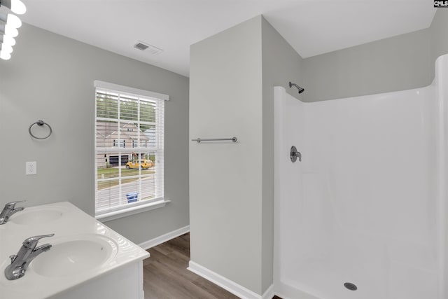 bathroom featuring walk in shower, a sink, wood finished floors, and visible vents