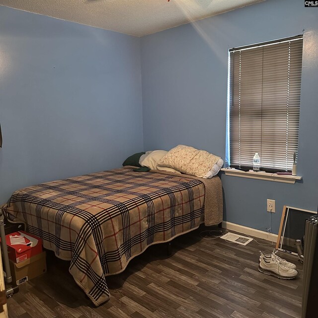 bedroom with a textured ceiling, wood finished floors, visible vents, and baseboards