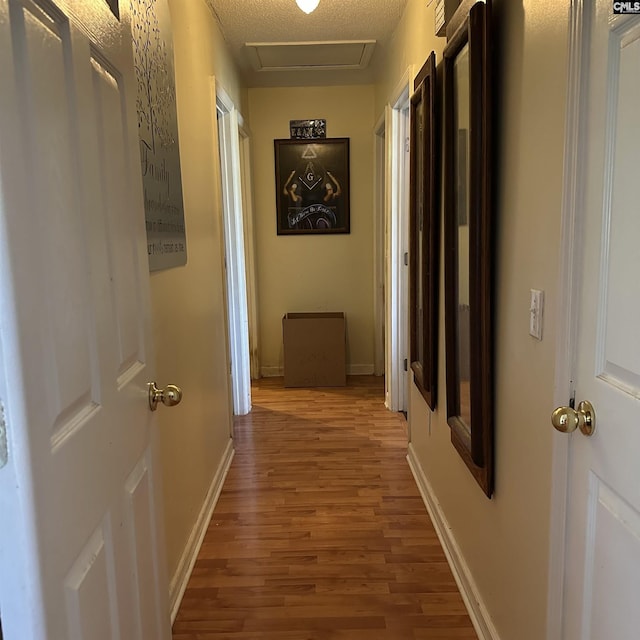 hall featuring attic access, wood finished floors, and baseboards