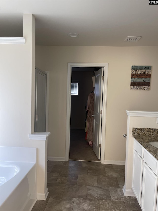 full bath with a garden tub, stone finish flooring, vanity, and baseboards