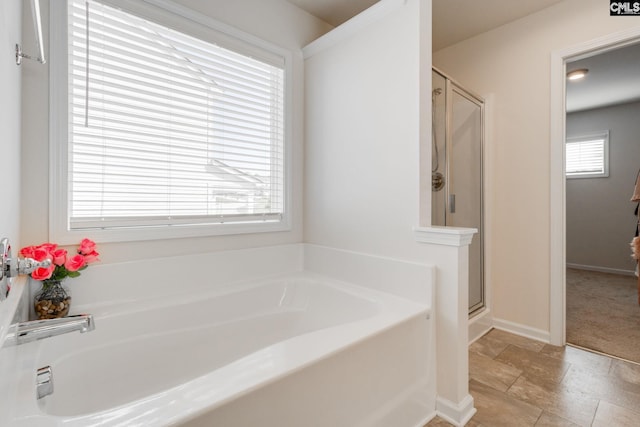 full bath with baseboards, stone finish flooring, a bath, and a shower stall