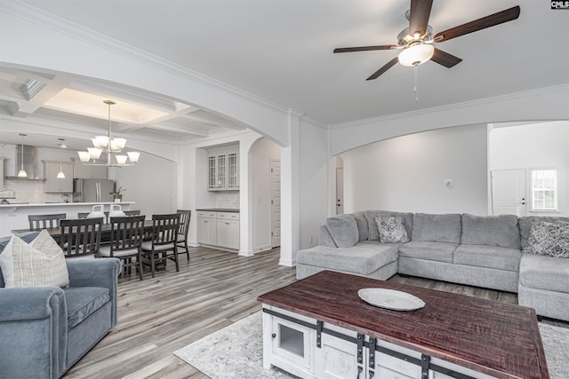 living room with arched walkways, ceiling fan with notable chandelier, light wood-style floors, and ornamental molding
