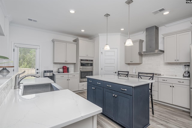 kitchen featuring stainless steel double oven, a kitchen island, wall chimney range hood, a sink, and visible vents