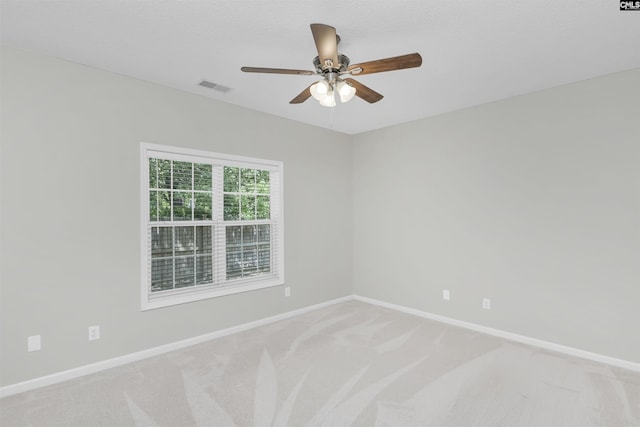 spare room featuring light colored carpet, visible vents, ceiling fan, and baseboards
