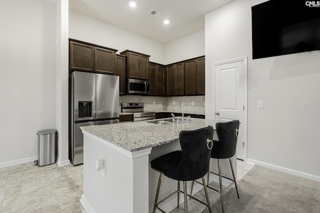 kitchen featuring a sink, visible vents, stainless steel appliances, dark brown cabinetry, and a kitchen bar