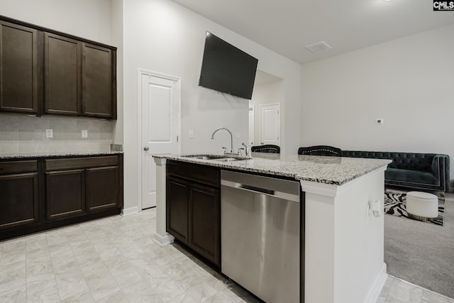 kitchen featuring stainless steel dishwasher, a sink, dark brown cabinets, light stone countertops, and an island with sink