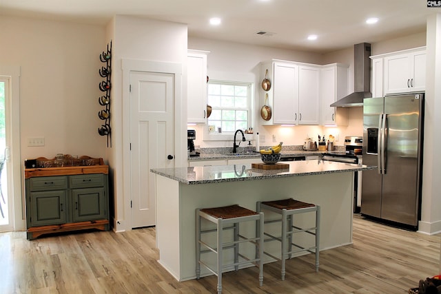 kitchen with wall chimney range hood, white cabinetry, stainless steel appliances, and a sink