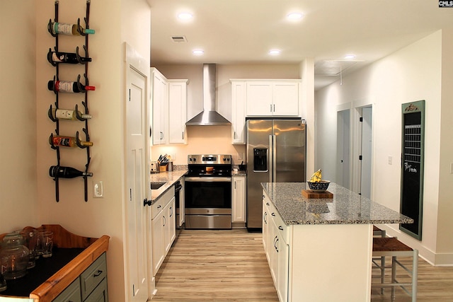 kitchen featuring stainless steel appliances, light wood-style floors, wall chimney range hood, a center island, and a kitchen breakfast bar