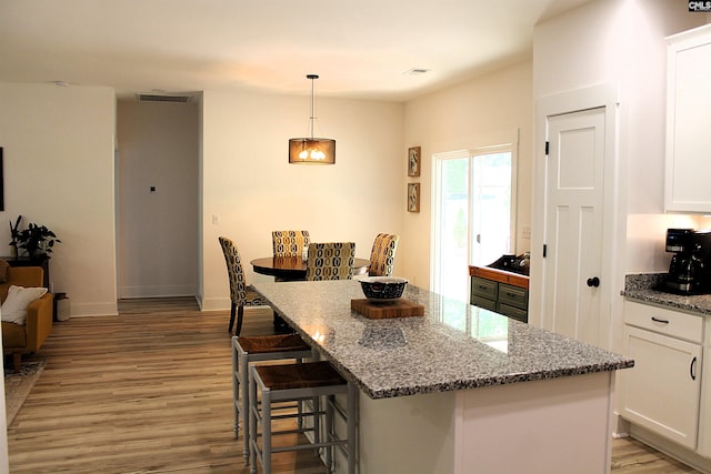 kitchen featuring light wood-style flooring, visible vents, a kitchen bar, and white cabinets