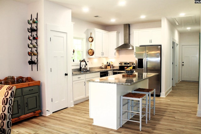 kitchen with stainless steel appliances, light wood finished floors, wall chimney range hood, and a sink