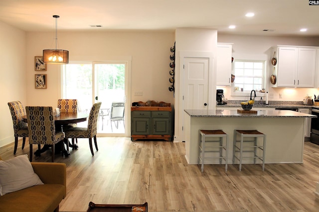 kitchen featuring dark stone countertops, white cabinets, a center island, a sink, and visible vents