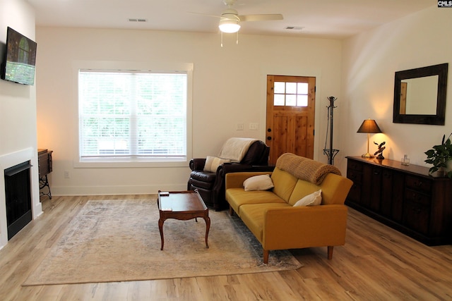 living area featuring visible vents, ceiling fan, a fireplace, and light wood-style flooring