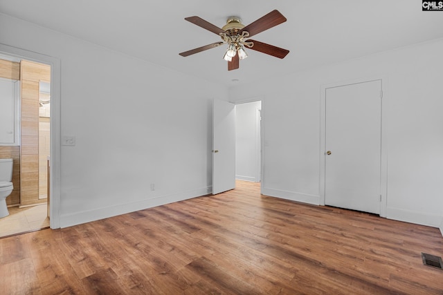 unfurnished bedroom with baseboards, visible vents, wood finished floors, and connected bathroom