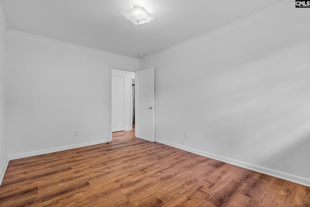 empty room featuring wood finished floors, ornamental molding, and baseboards