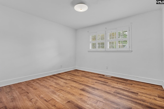 unfurnished room with baseboards, visible vents, and wood finished floors