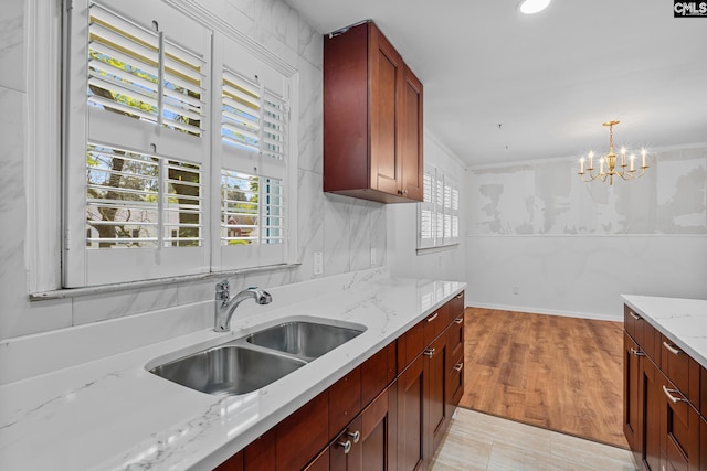 kitchen with light stone counters, a sink, an inviting chandelier, light wood-type flooring, and decorative light fixtures