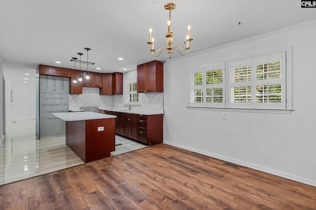 kitchen with tasteful backsplash, light wood-style floors, a kitchen island, baseboards, and an inviting chandelier