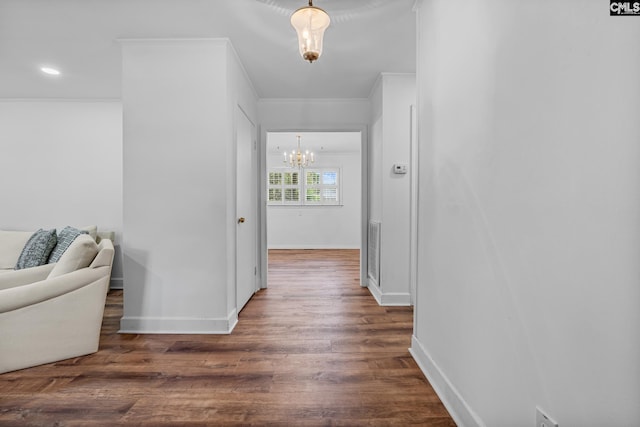 hallway with dark wood-style floors, a notable chandelier, visible vents, baseboards, and ornamental molding