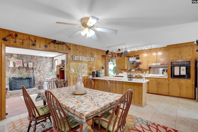 dining space featuring light tile patterned floors, ceiling fan, wooden walls, and a textured ceiling