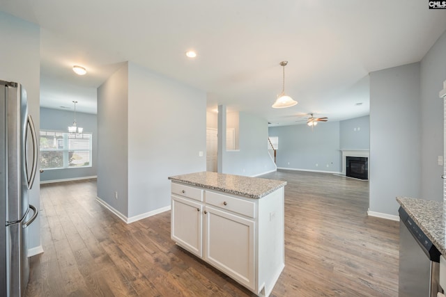 kitchen with stainless steel appliances, white cabinets, ceiling fan with notable chandelier, a glass covered fireplace, and baseboards
