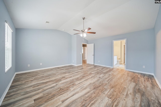 unfurnished bedroom with baseboards, ensuite bathroom, light wood-style flooring, and vaulted ceiling