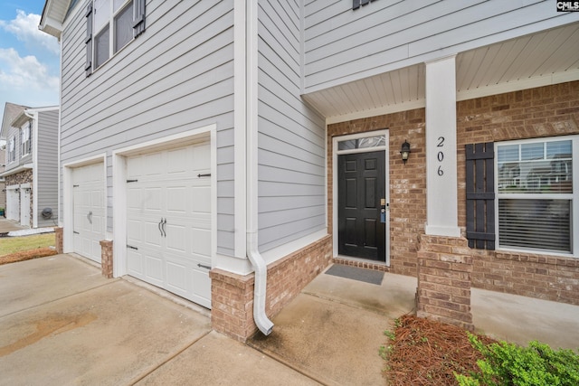doorway to property featuring driveway, brick siding, and a garage
