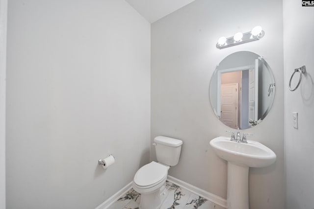 half bath with a sink, toilet, marble finish floor, and baseboards