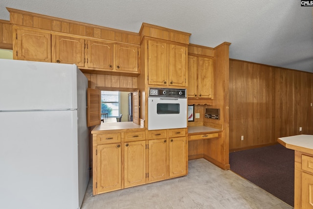 kitchen featuring white appliances, brown cabinetry, wooden walls, light countertops, and a textured ceiling