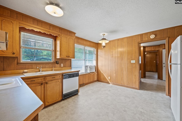 kitchen featuring white appliances, a textured ceiling, light countertops, a sink, and wooden walls