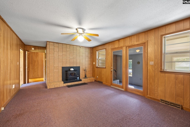 unfurnished living room featuring wooden walls, a ceiling fan, visible vents, and a textured ceiling