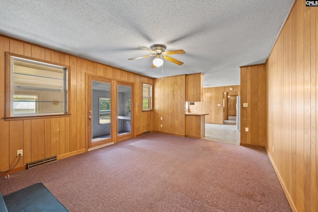 unfurnished living room featuring carpet flooring, wooden walls, a ceiling fan, visible vents, and baseboards