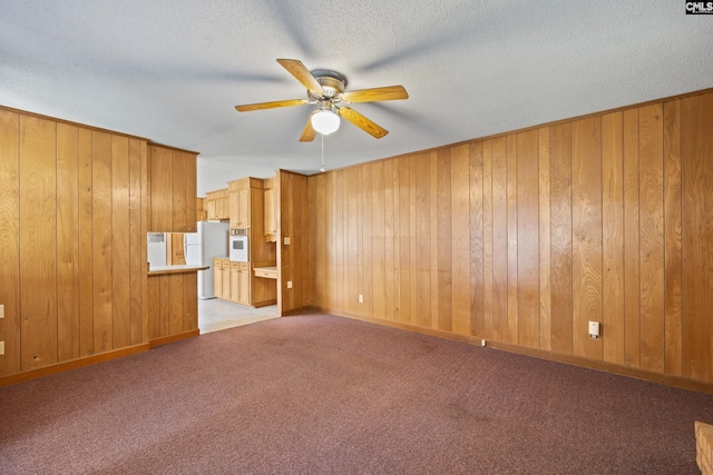 unfurnished living room with a ceiling fan, wooden walls, and light colored carpet