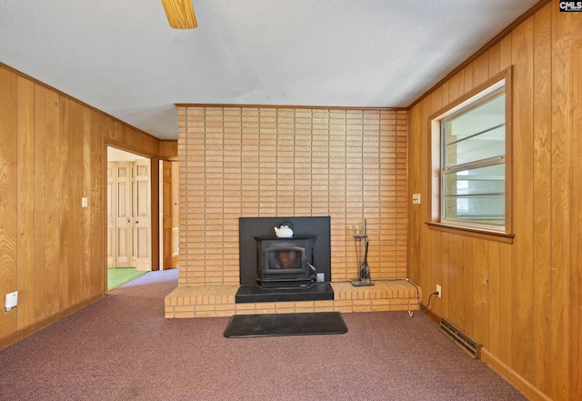 unfurnished living room with a wood stove, wooden walls, baseboards, a textured ceiling, and carpet floors