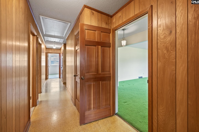 hallway featuring attic access, a textured ceiling, wood walls, and baseboards