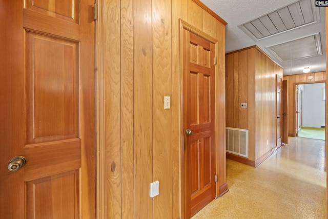 corridor with attic access, wooden walls, visible vents, baseboards, and a textured ceiling