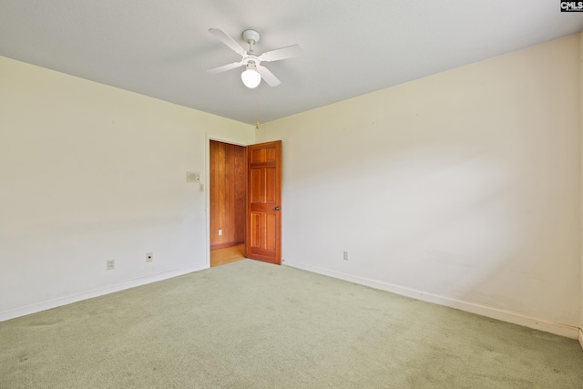 spare room featuring light colored carpet, a ceiling fan, and baseboards
