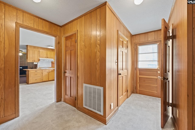 corridor featuring visible vents, ornamental molding, a textured ceiling, and wood walls
