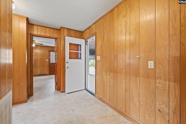 interior space featuring light floors, wood walls, ornamental molding, visible vents, and a textured ceiling