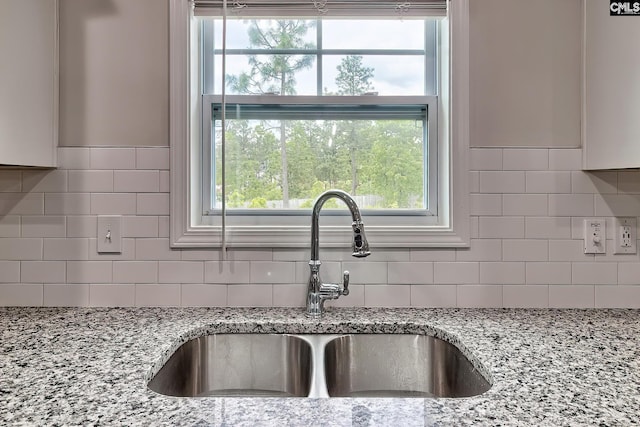 kitchen featuring light stone counters, backsplash, and a sink