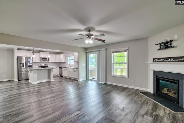 unfurnished living room with a sink, dark wood-style flooring, ceiling fan, a glass covered fireplace, and baseboards