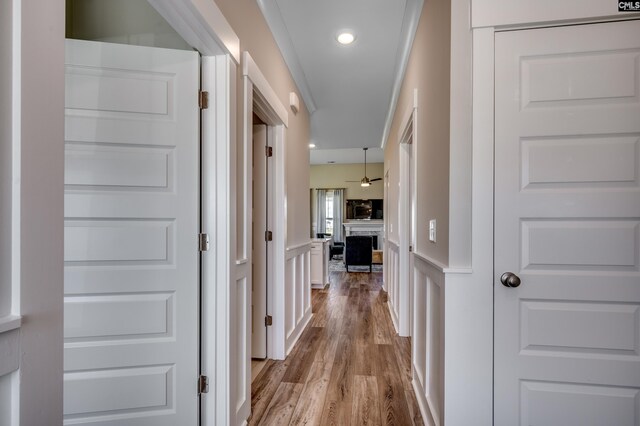 corridor featuring light wood-type flooring, a wainscoted wall, and a decorative wall