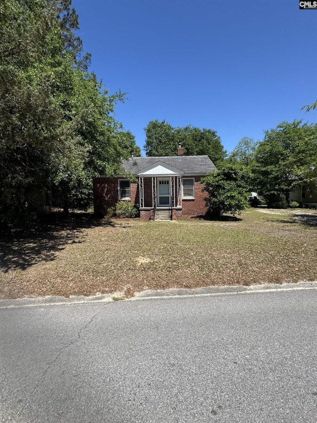 view of front of home featuring a front lawn, a chimney, and brick siding