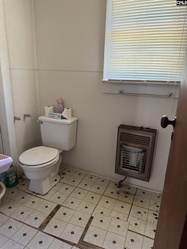 half bathroom with tile patterned floors, heating unit, toilet, and tile walls