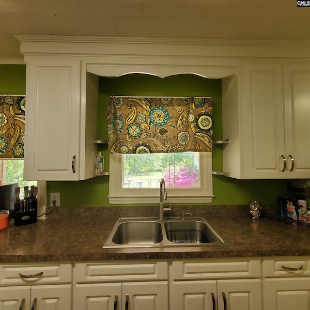 kitchen featuring dark countertops, a healthy amount of sunlight, white cabinets, and a sink
