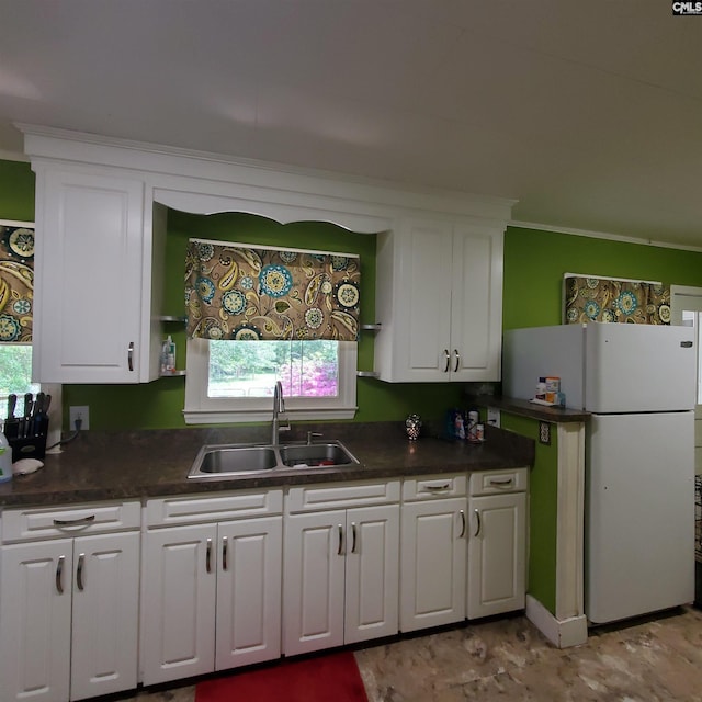 kitchen with dark countertops, a sink, white cabinets, and freestanding refrigerator