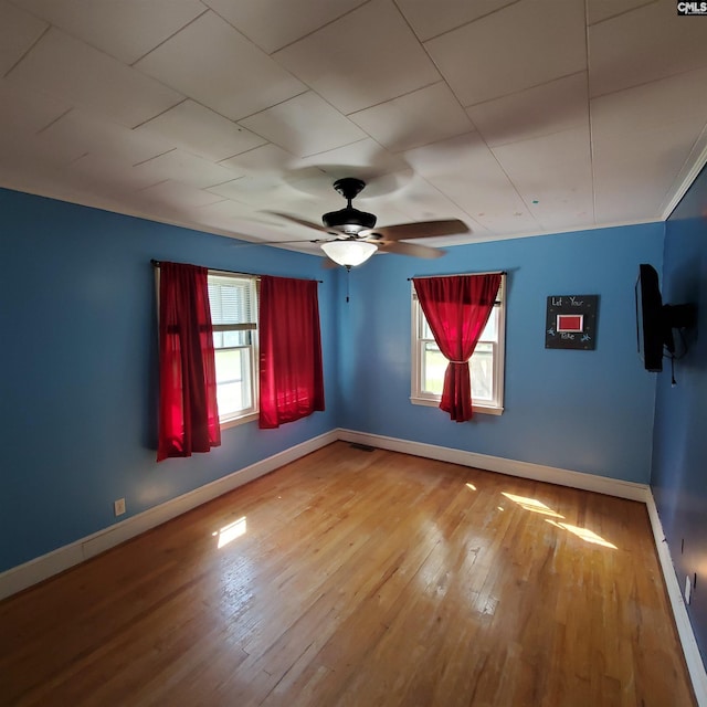 empty room with wood-type flooring, a ceiling fan, and baseboards