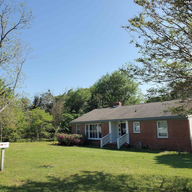 view of front of home featuring a front lawn, a chimney, and brick siding