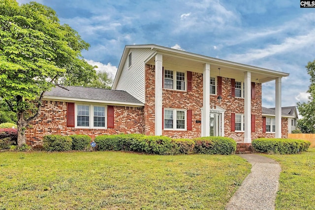 greek revival inspired property featuring a front yard, fence, and brick siding